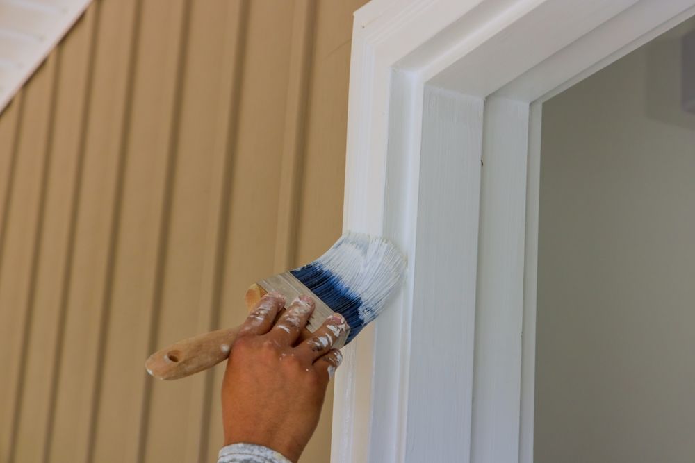 Person painting white trim around a door with a paintbrush — TMP Painting Services in Beaconsfield, QLD