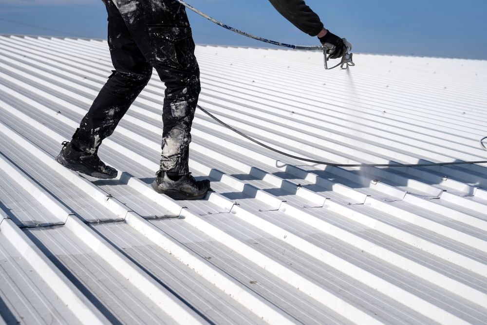 Person spraying white paint on a corrugated metal roof — TMP Painting Services in Beaconsfield, QLD