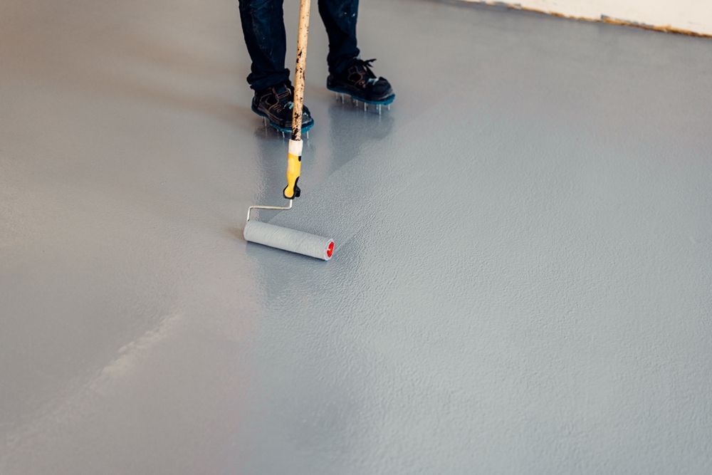 Person using a paint roller to apply gray coating to a floor — TMP Painting Services in Beaconsfield, QLD