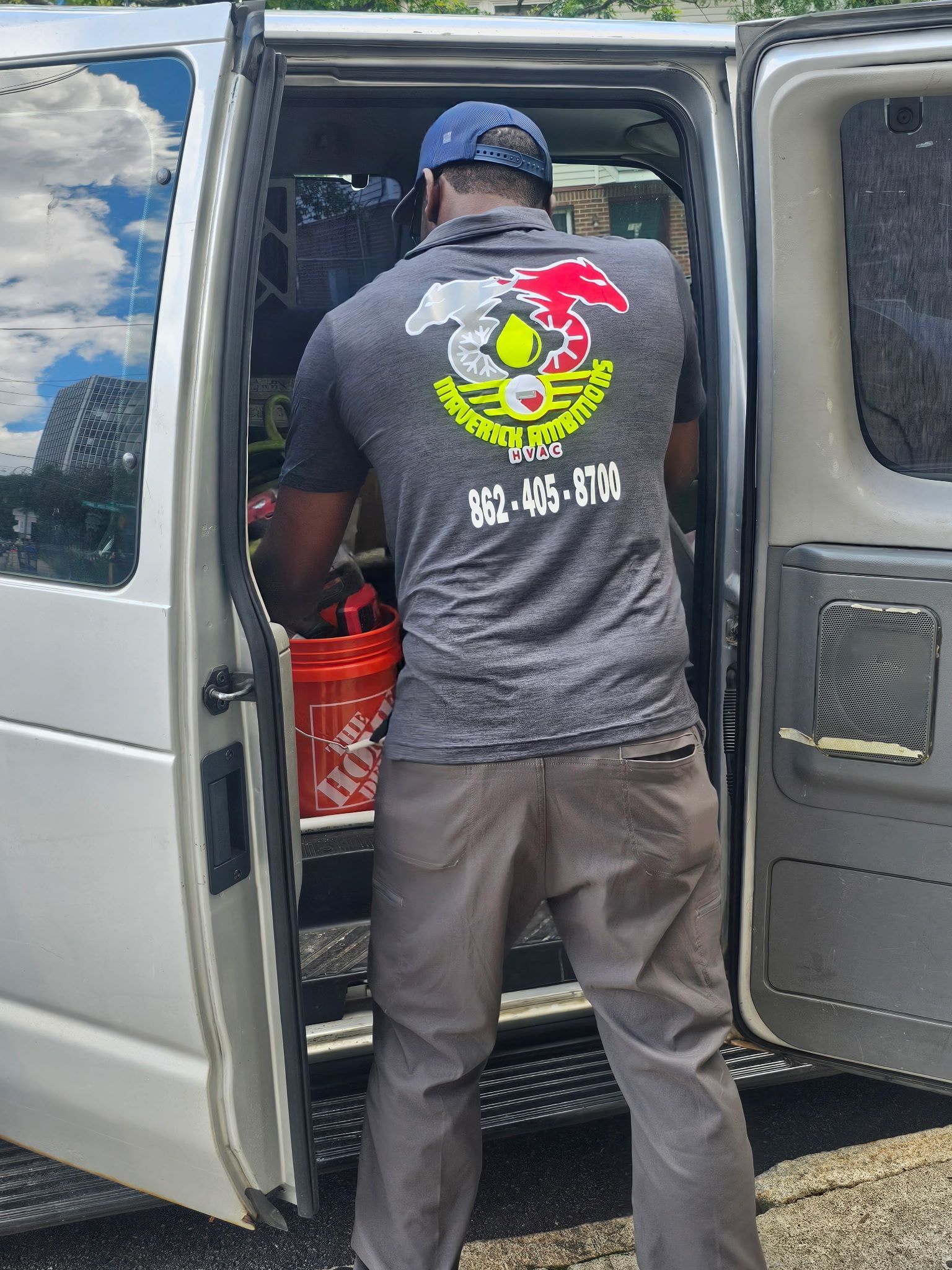 Man unloading red crates from a white van with open side doors outdoors under a cloudy sky