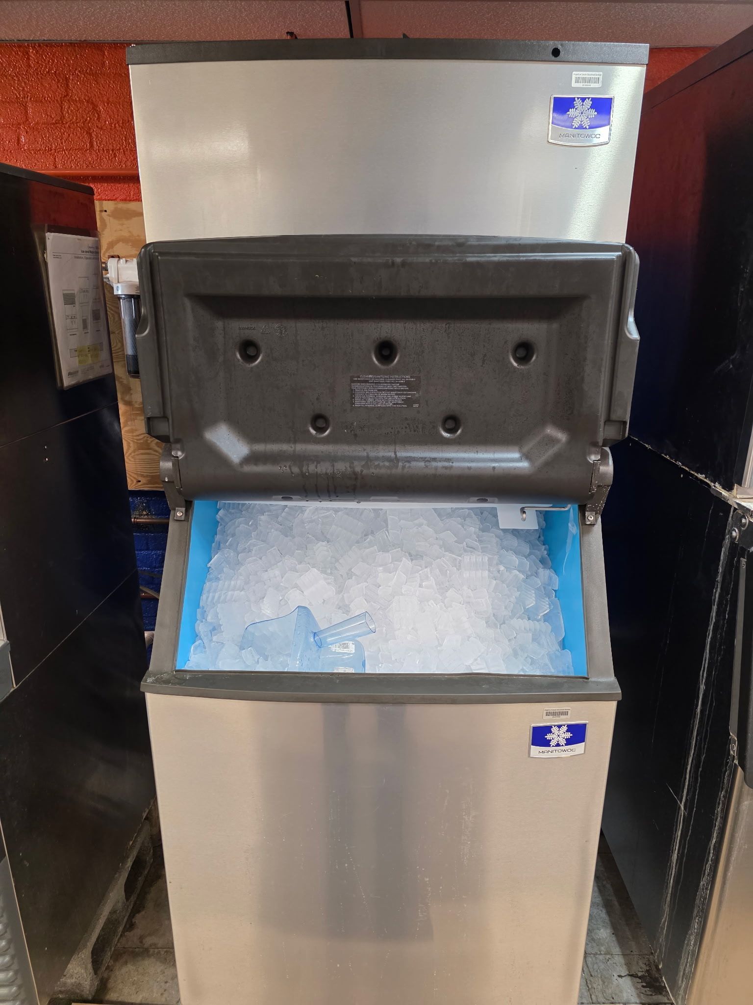 Front view of a stainless steel commercial ice machine with the bin door open and ice visible inside.