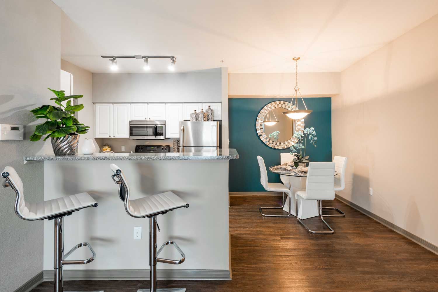 Open-concept kitchen with white cabinets, stainless appliances, granite counter, and a teal-accent dining area.