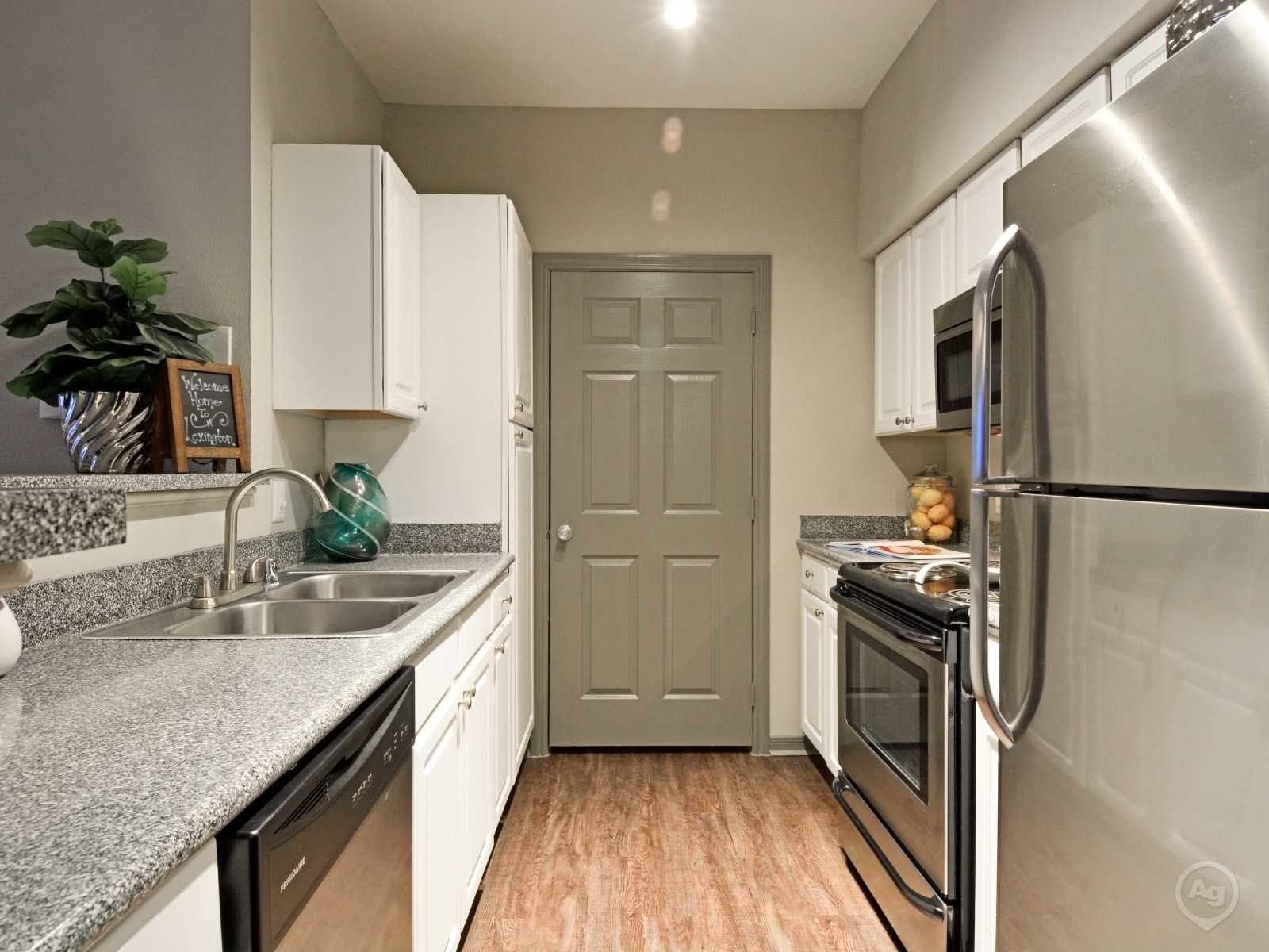 Galley-style kitchen in a modern apartment with white cabinets, granite countertops, and stainless steel appliances.