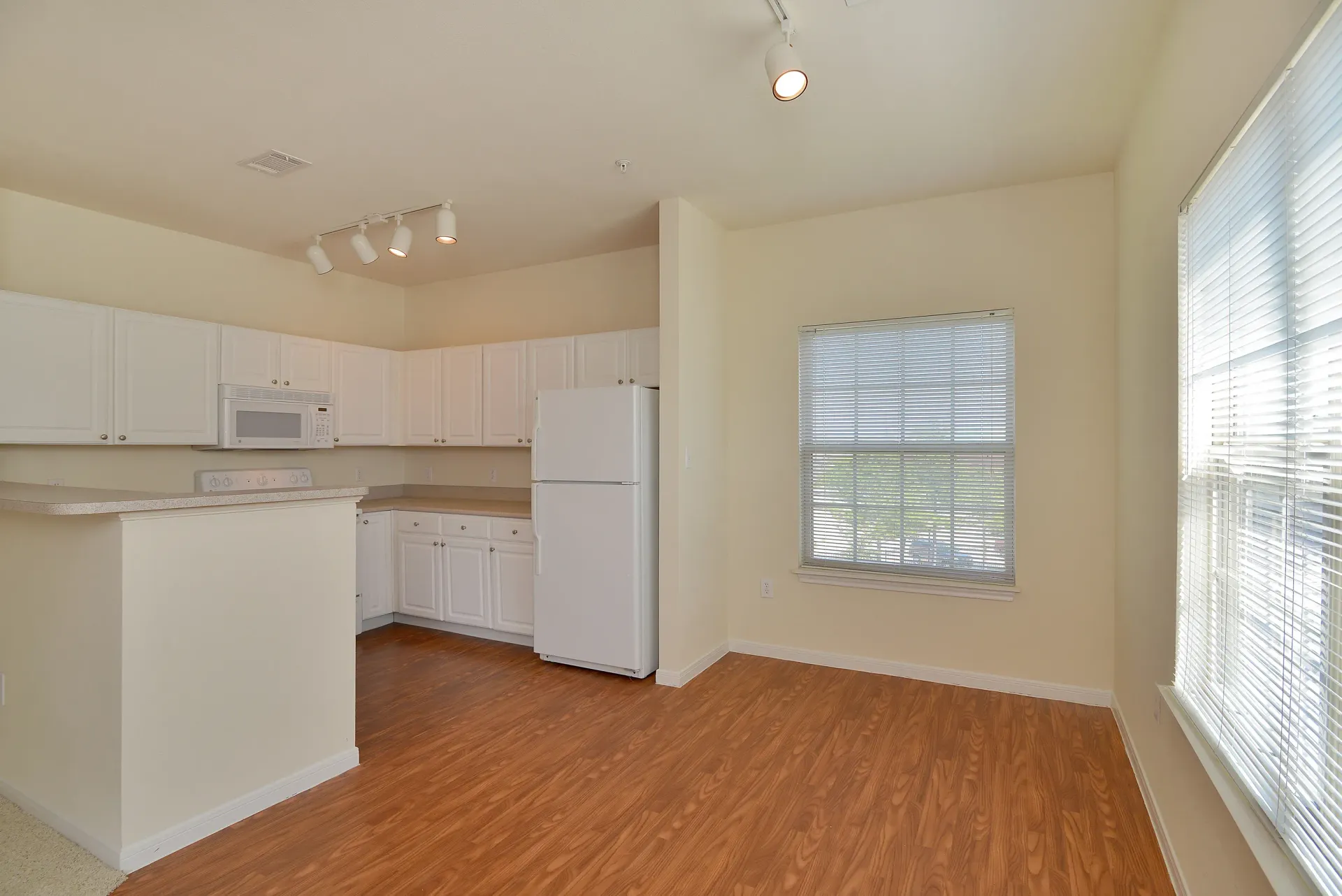Bright apartment kitchen with white cabinets, appliances, and a large window with blinds.