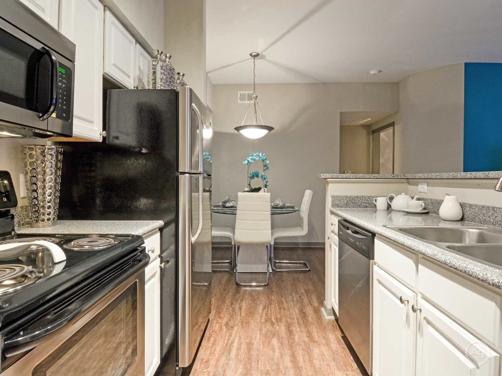 Apartment kitchen with white cabinets, stainless steel appliances, and a small dining table.