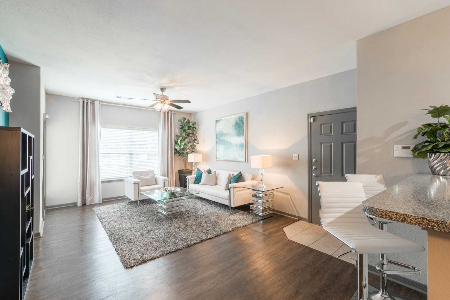 Bright living room with white sofa, glass coffee table, and bar seating near the kitchen.