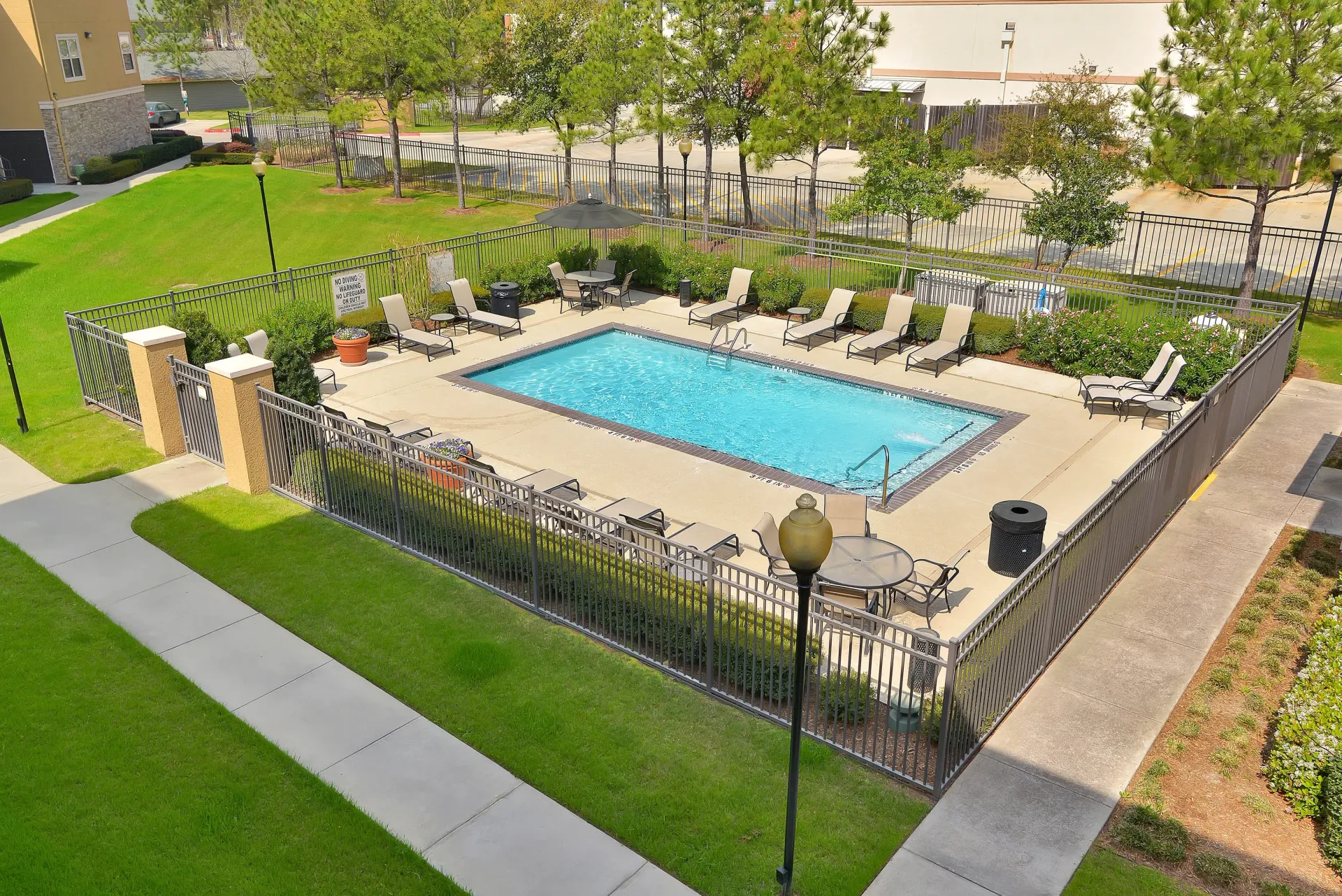 Outdoor apartment community pool with lounge chairs, umbrellas, and a surrounding fence.