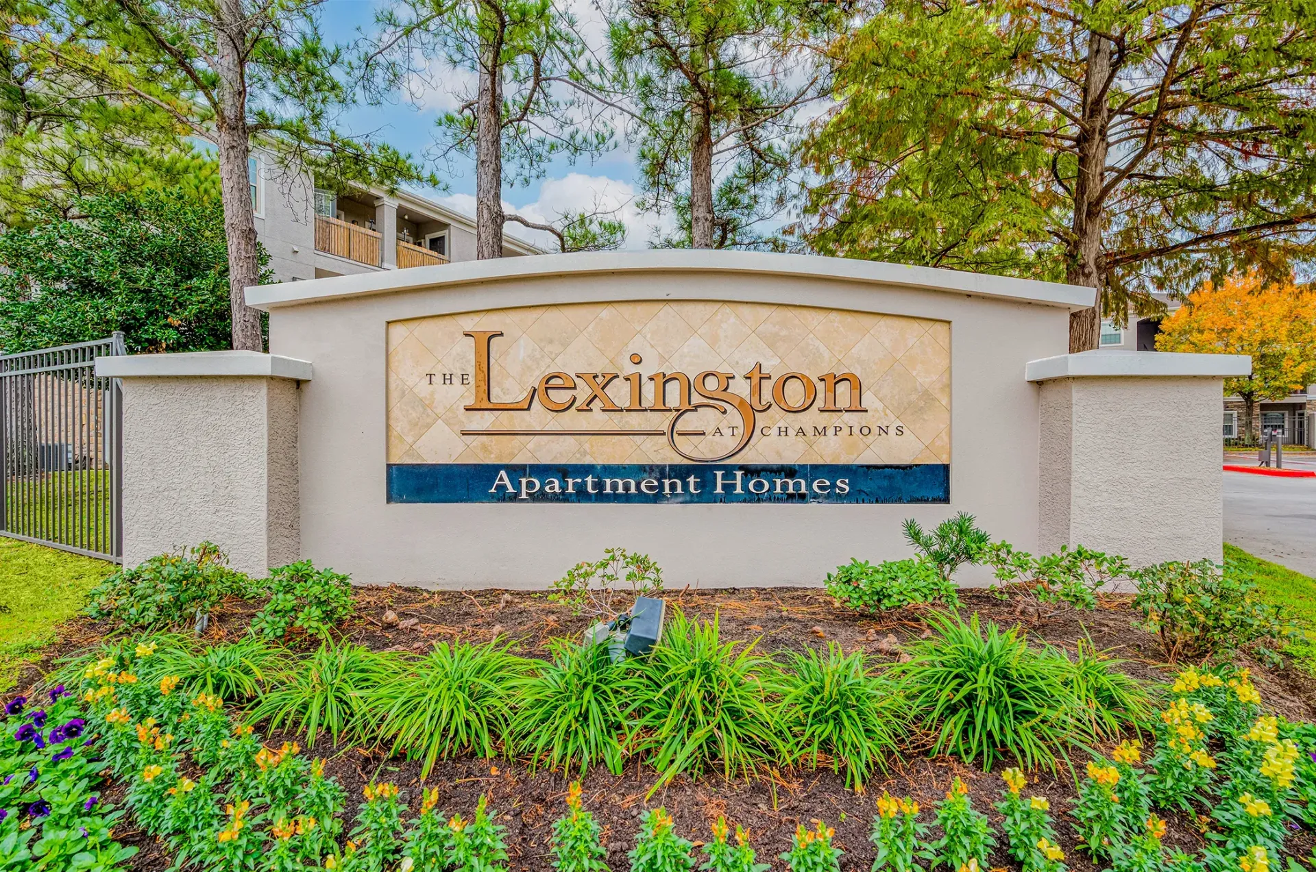 Curved entrance sign for The Lexington at Champions Apartments with landscaping.