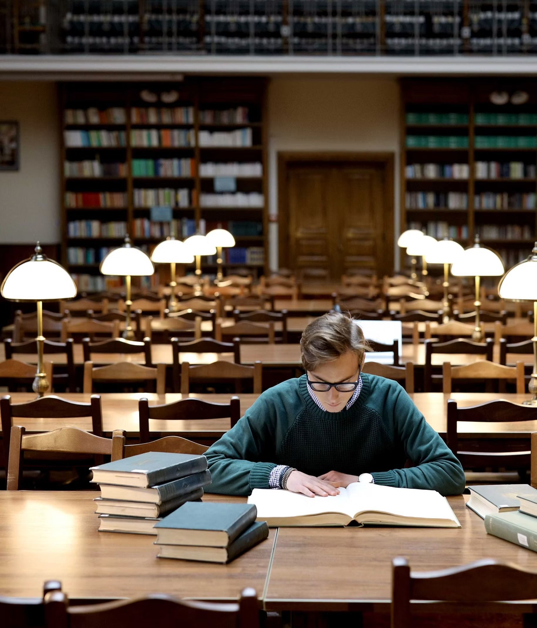 Man reading in a library with books, lamps, and bookshelves in the background.