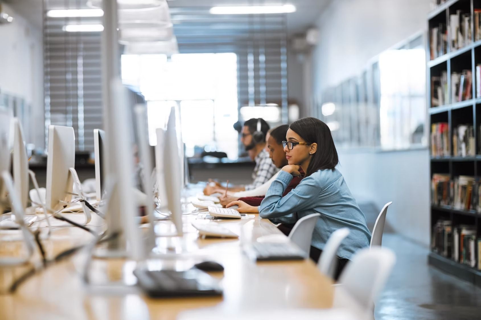 People at computers in a library, one woman looking at the screen.