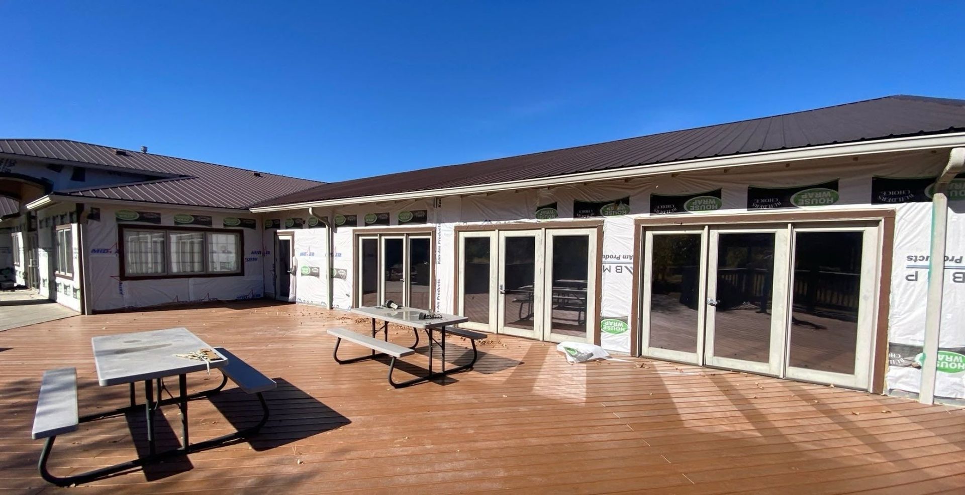 Patio with picnic tables in front of a long house with large glass doors under a blue sky