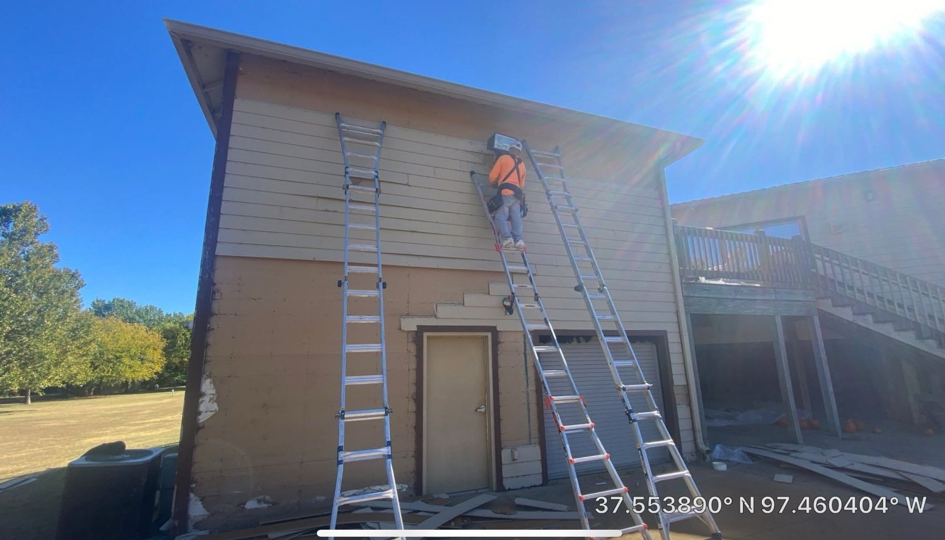 Worker on a ladder painting the exterior of a building in bright sunlight