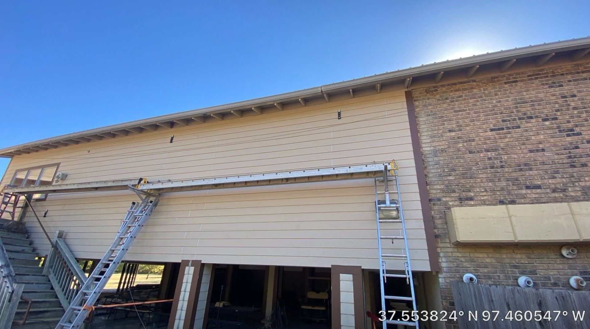 Exterior of a brick building with an open garage door and two ladders leaning against the wall.