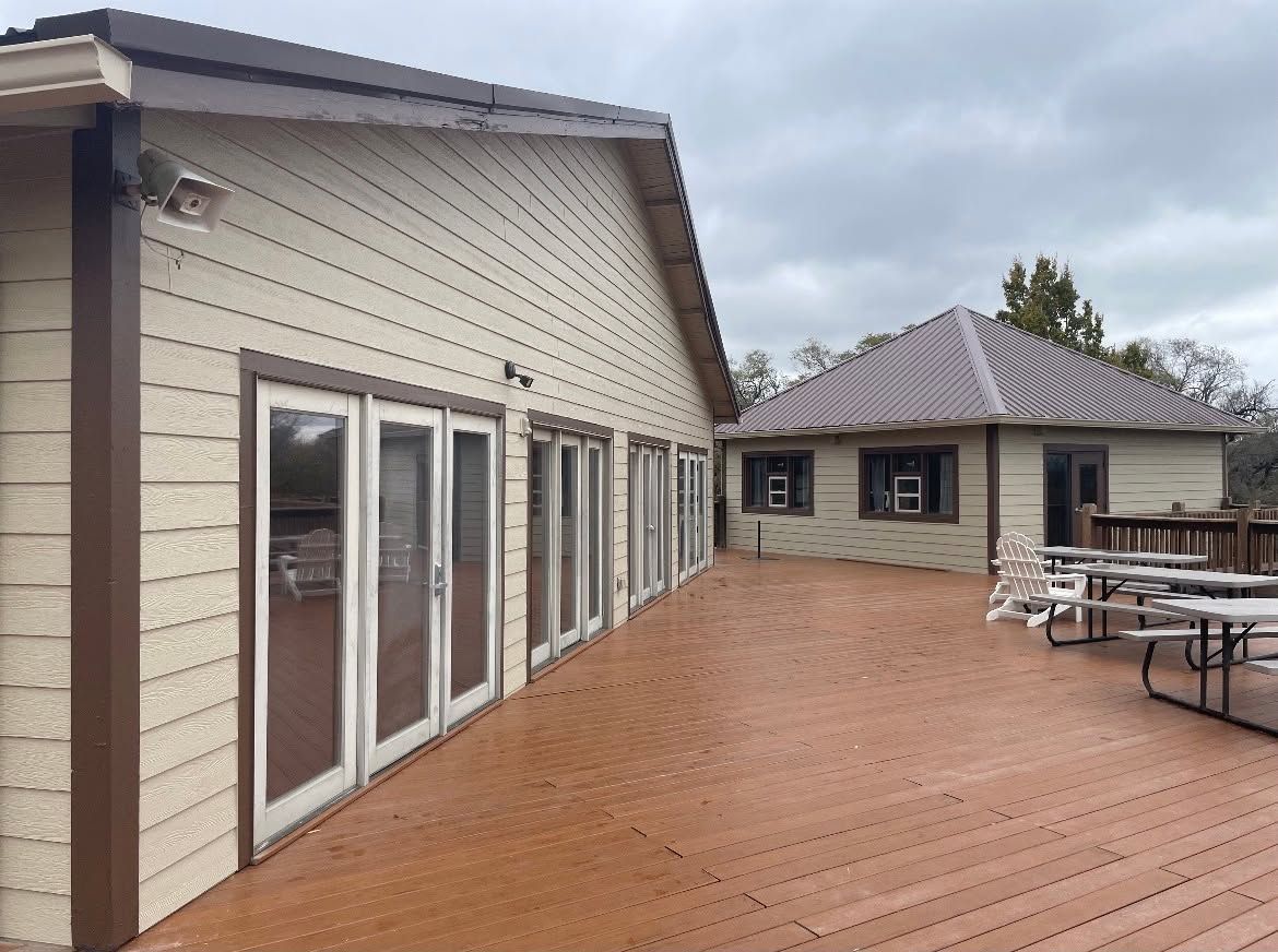 Wide wooden deck beside beige house with glass doors, outdoor seating, and a small outbuilding.