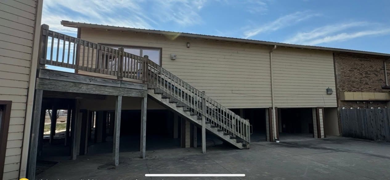 Empty parking lot beside a tan building with a wooden stairway and elevated deck.
