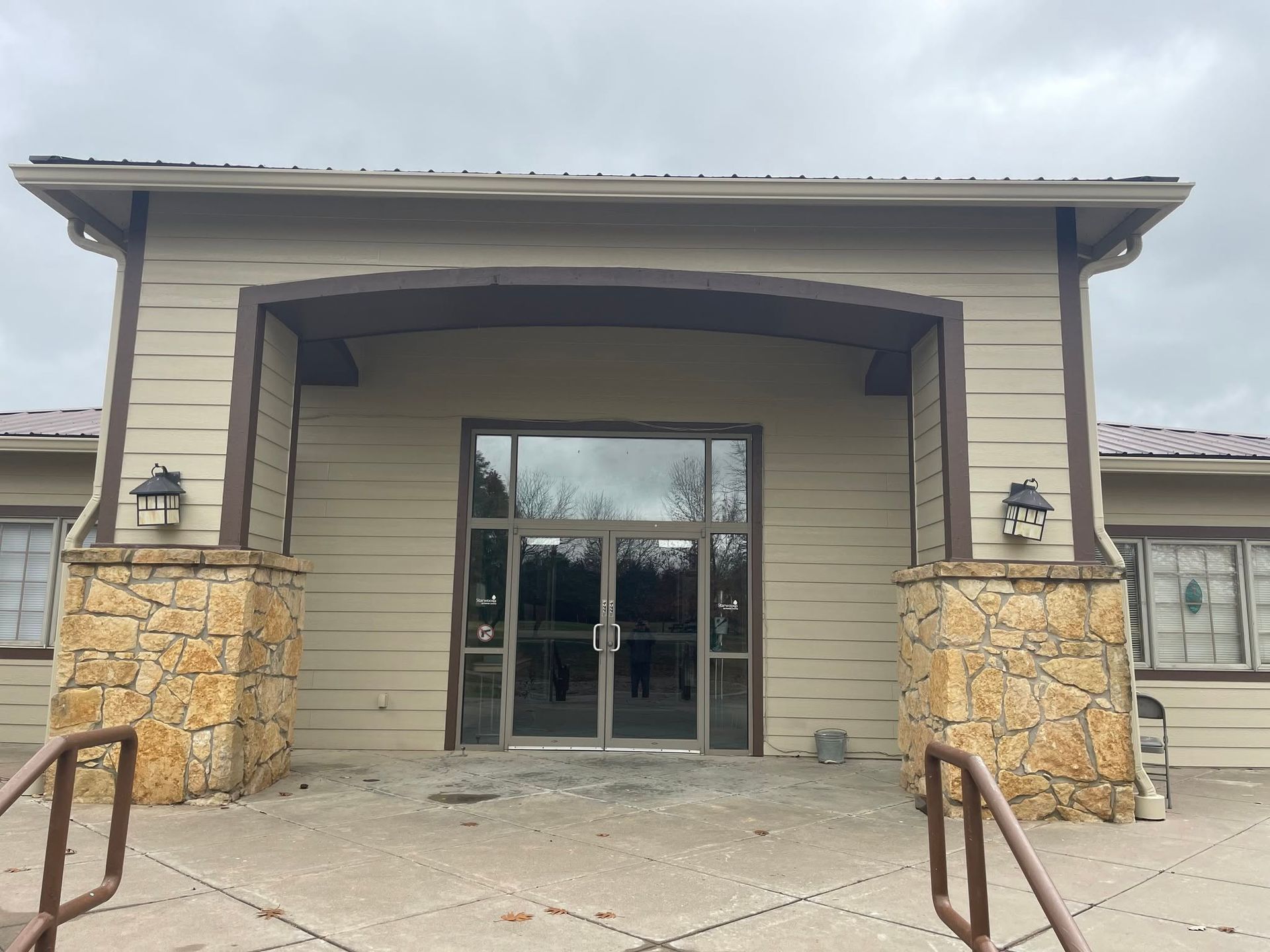 Building entrance with glass doors, stone pillars, and a covered entryway under a cloudy sky