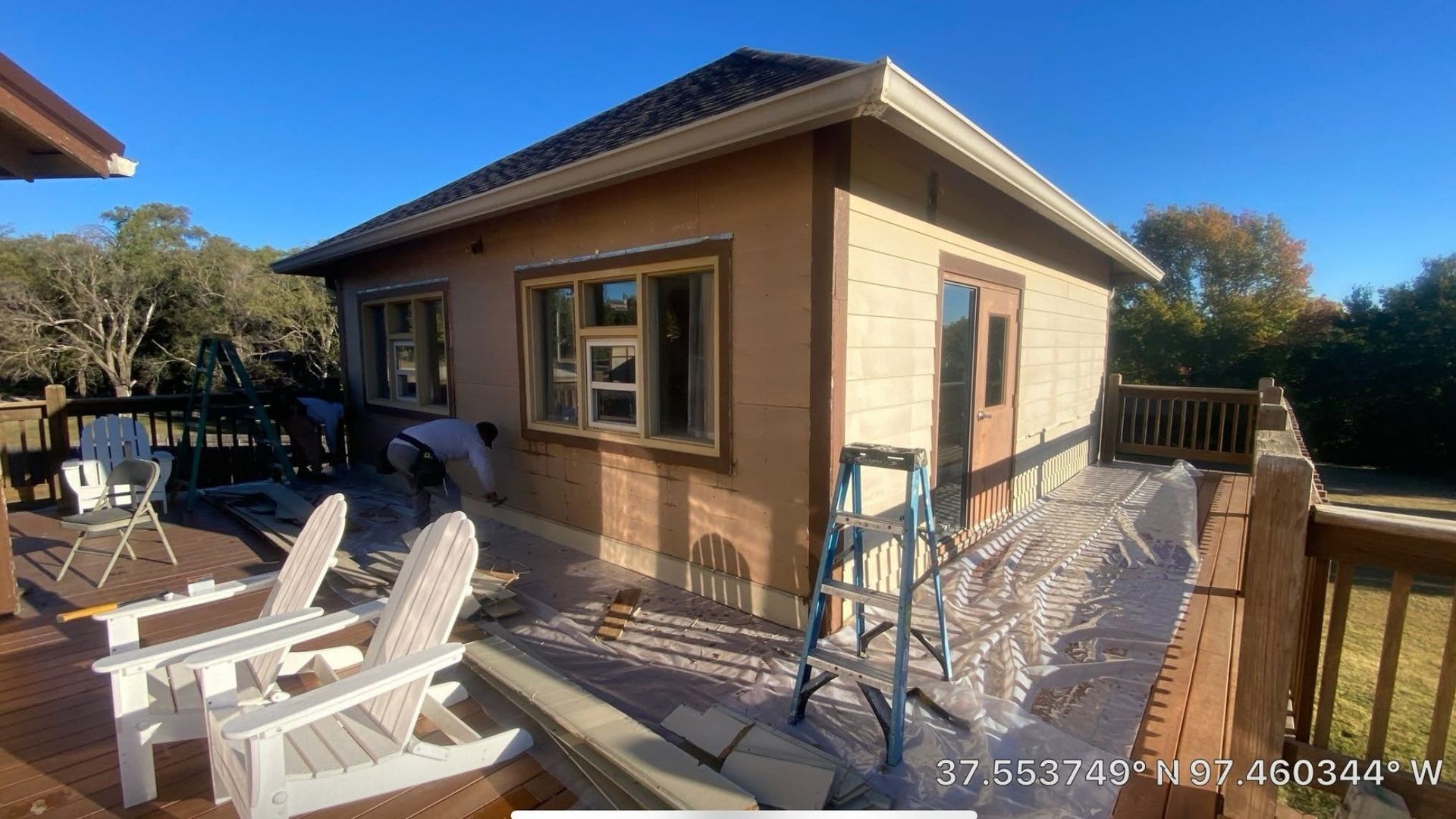 Small tan house with a blue roof, patio chairs, and a metal ramp under a sunny sky