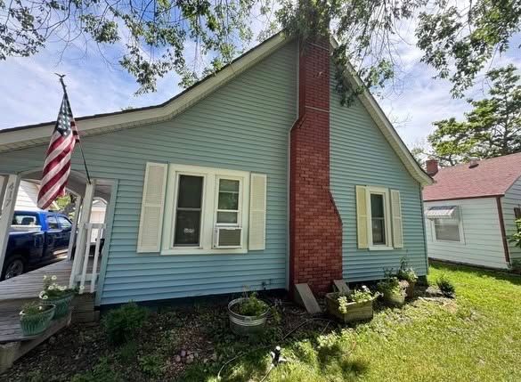 Small mint-green house with white shutters, red brick chimney, and an American flag by the porch