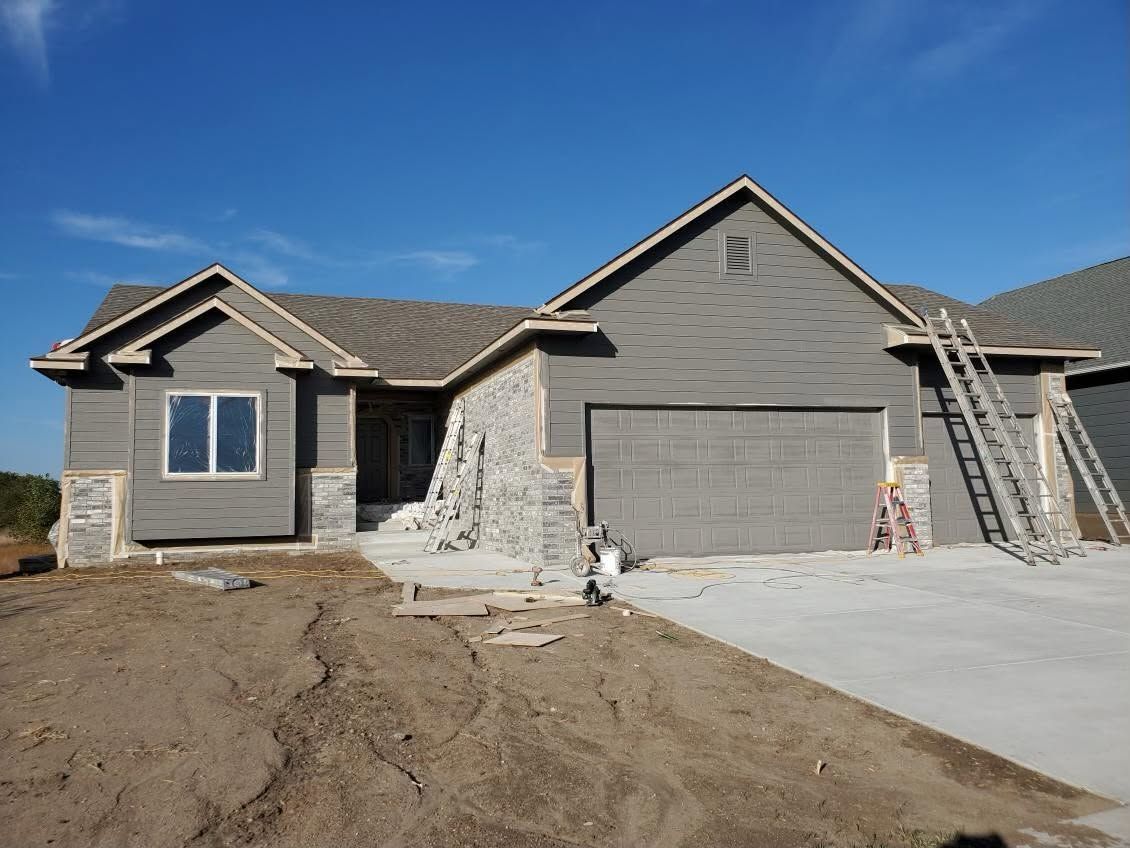 New gray house under construction with unfinished driveway and dirt lot in front
