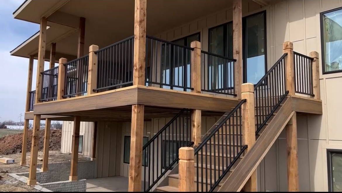 Two-story building with tan walls, black railings, and exterior stairs on a dirt lot.