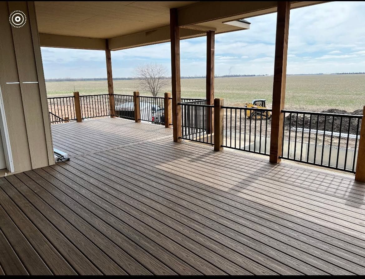 Covered wooden porch overlooking open fields with railings and posts