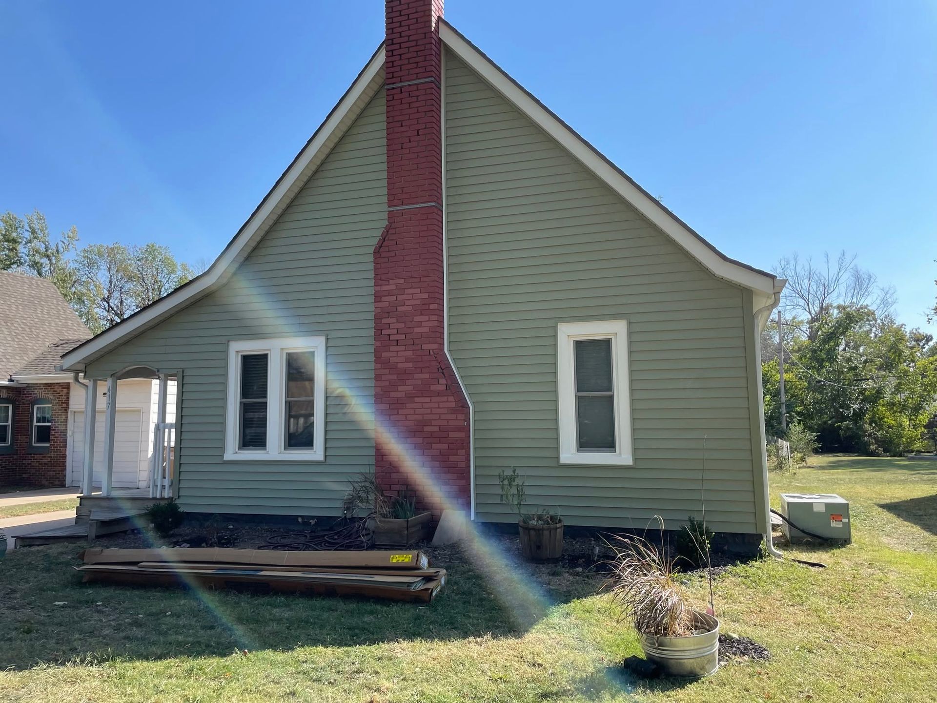 Small green house with red chimney, white-trimmed windows, and a front porch in a grassy yard.