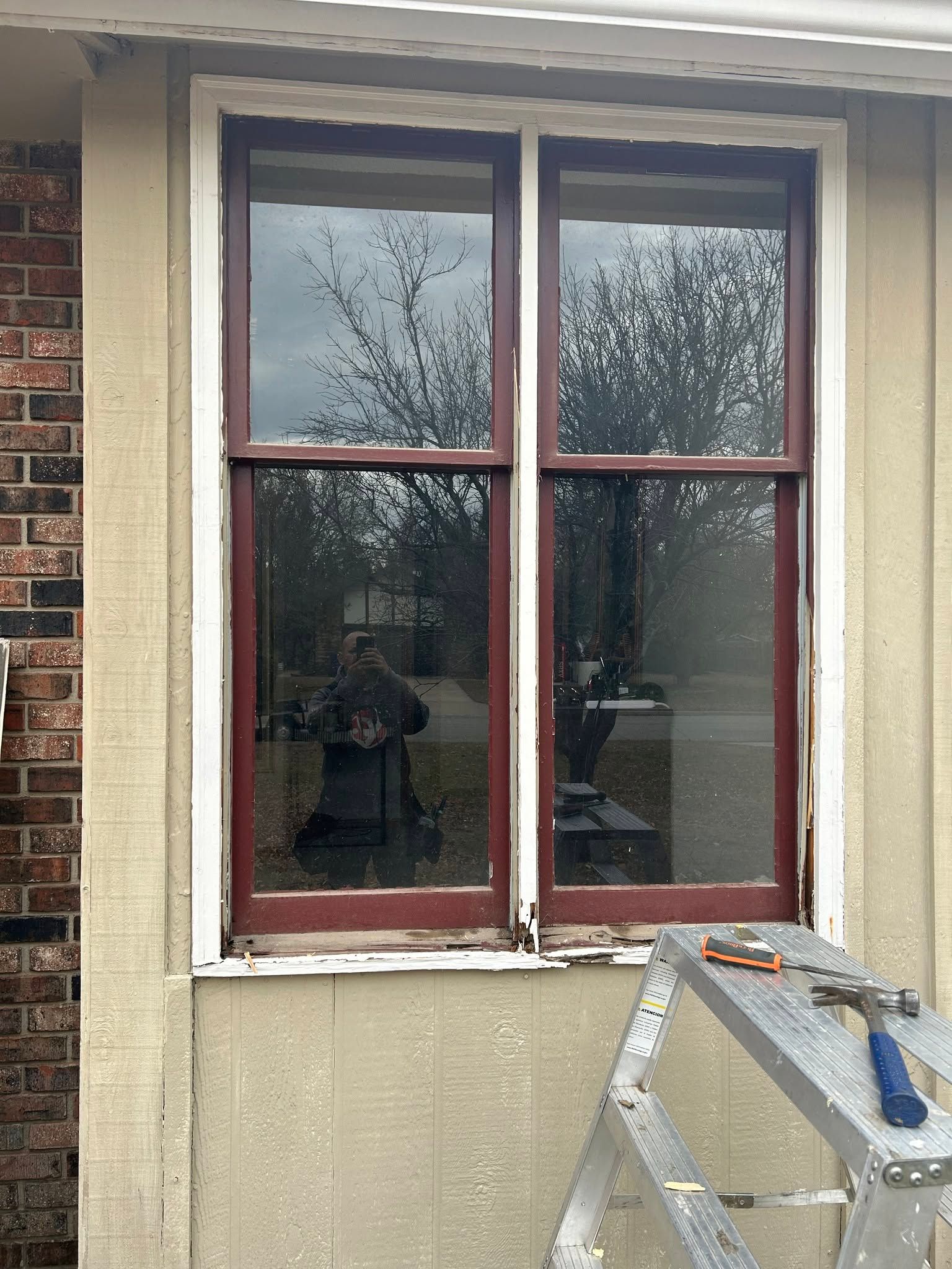Closed red-trimmed window on a brick house wall, with a ladder leaning below it.