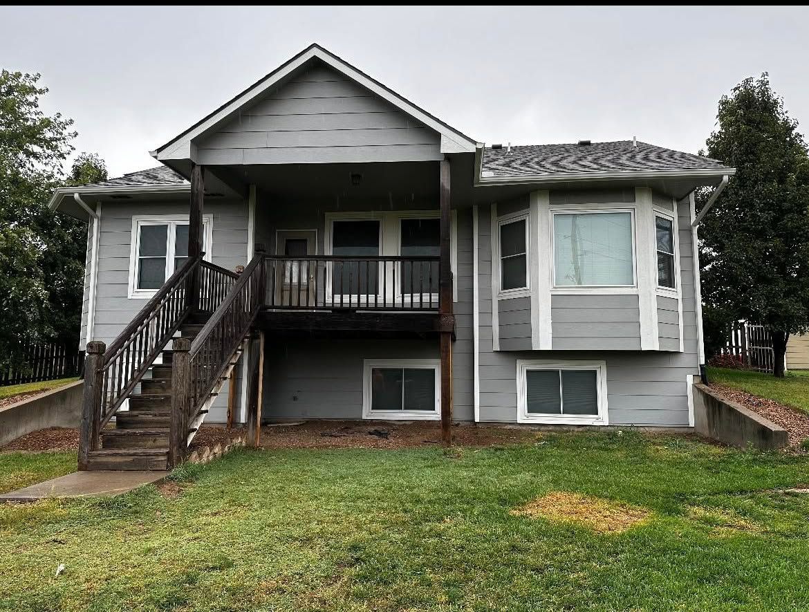 Gray house with front porch, exterior stairs, and a grassy yard under overcast skies
