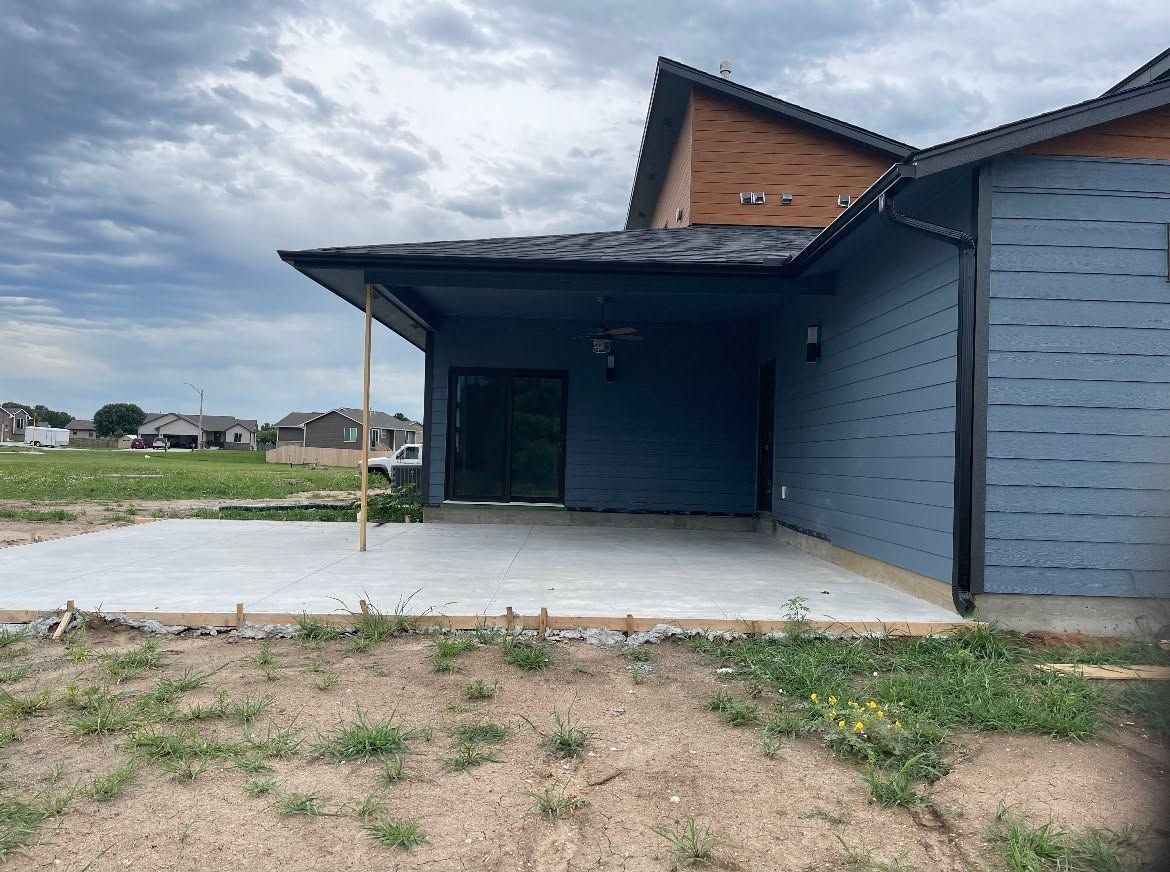 Modern house exterior with blue siding, covered porch, and bare dirt yard