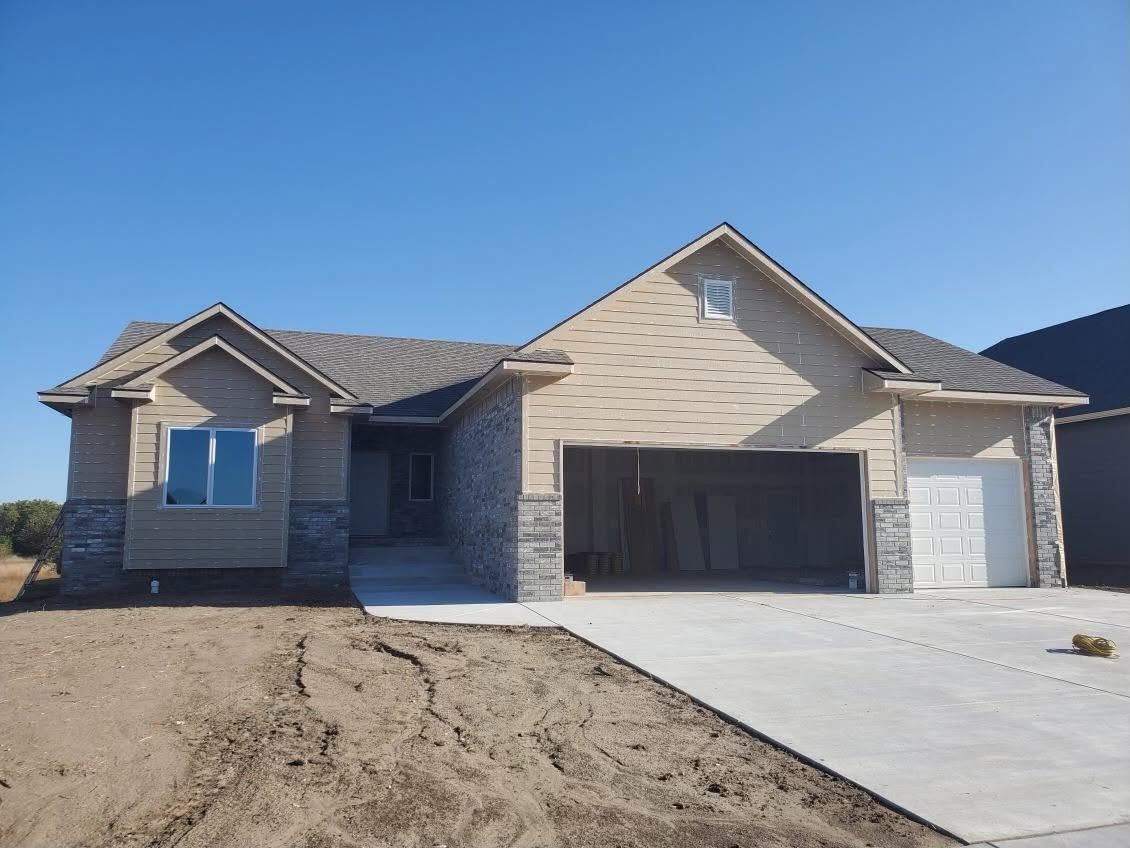 New suburban house under construction with driveway and dirt front yard under a clear blue sky