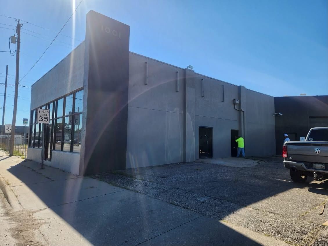 Gray commercial building with glass storefront and a person in a neon vest near the entrance