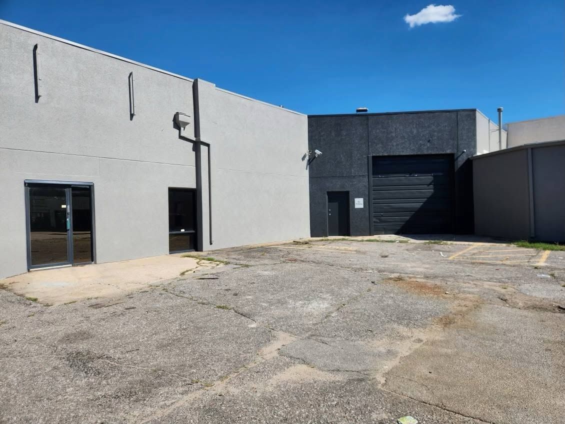 Gray industrial building with a gravel lot and a large dark garage door under a blue sky