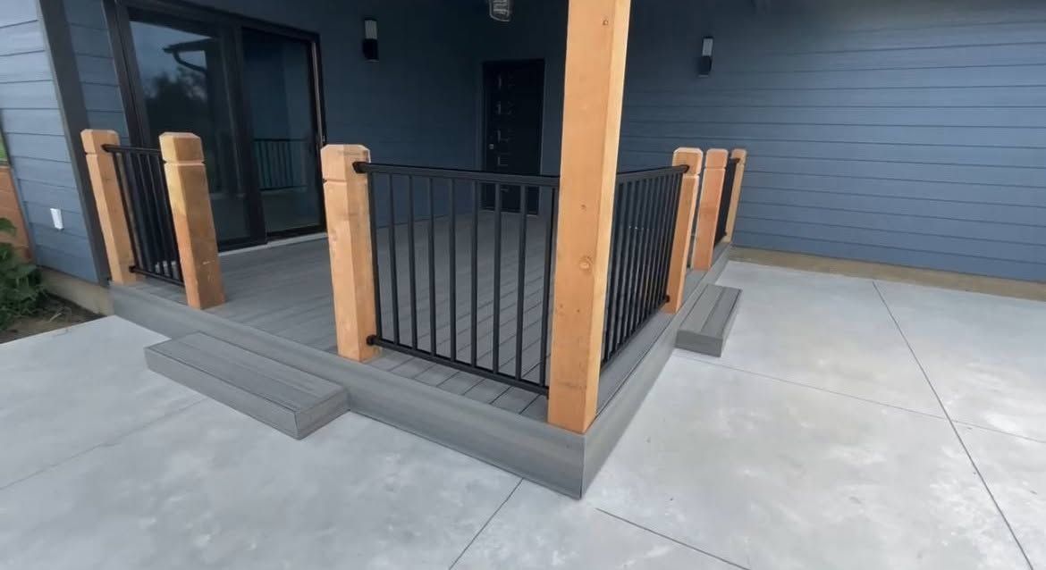 Front porch with black railing, wooden posts, and concrete steps leading to a dark entryway.