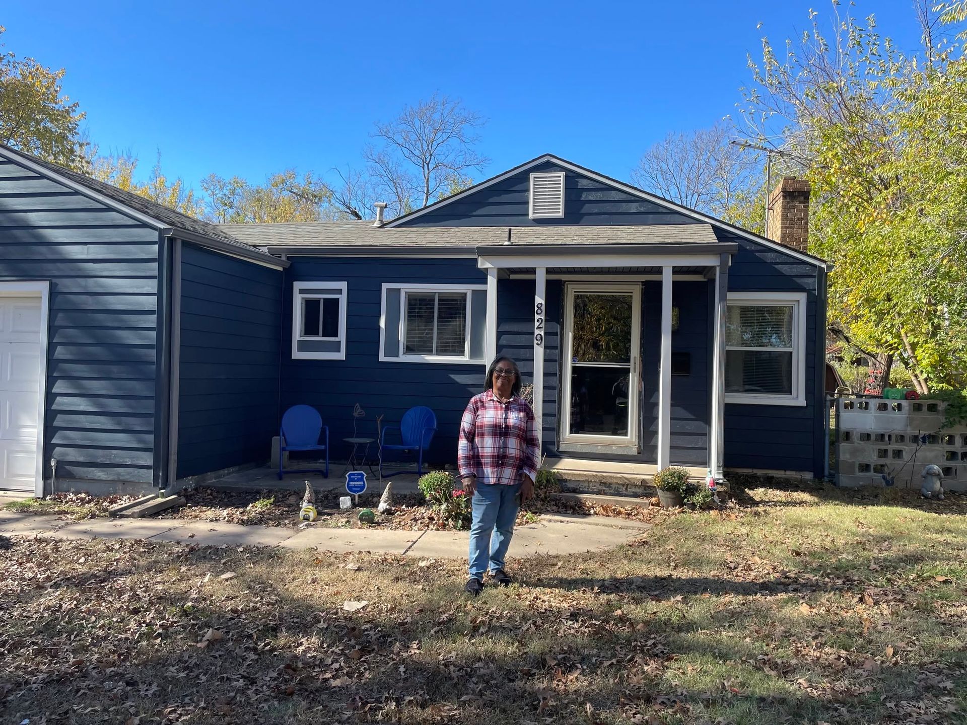 Person standing in front of a dark blue house with a small porch and two chairs on a sunny day