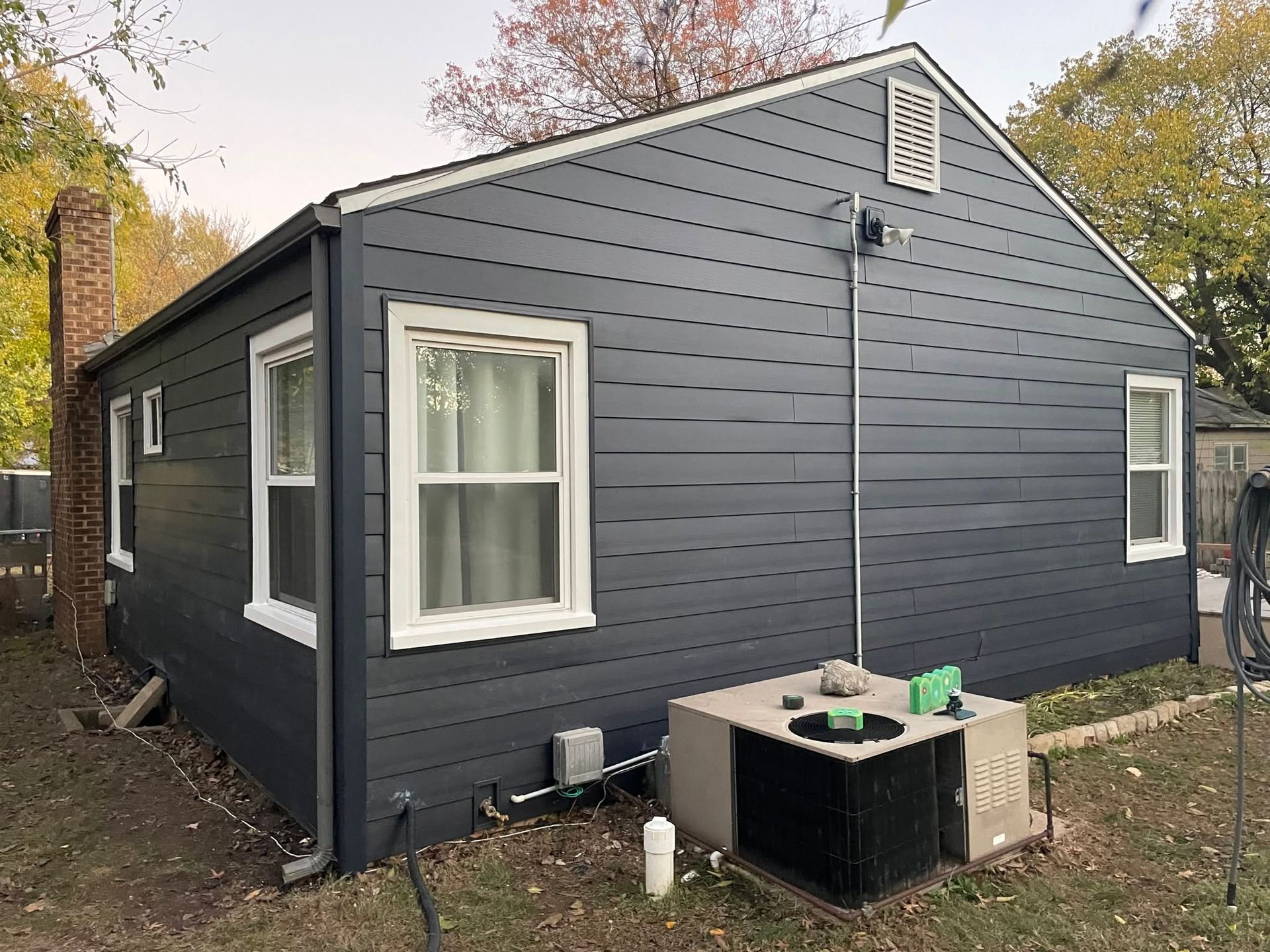 Dark gray house exterior with white-trimmed windows and a small utility unit in the yard