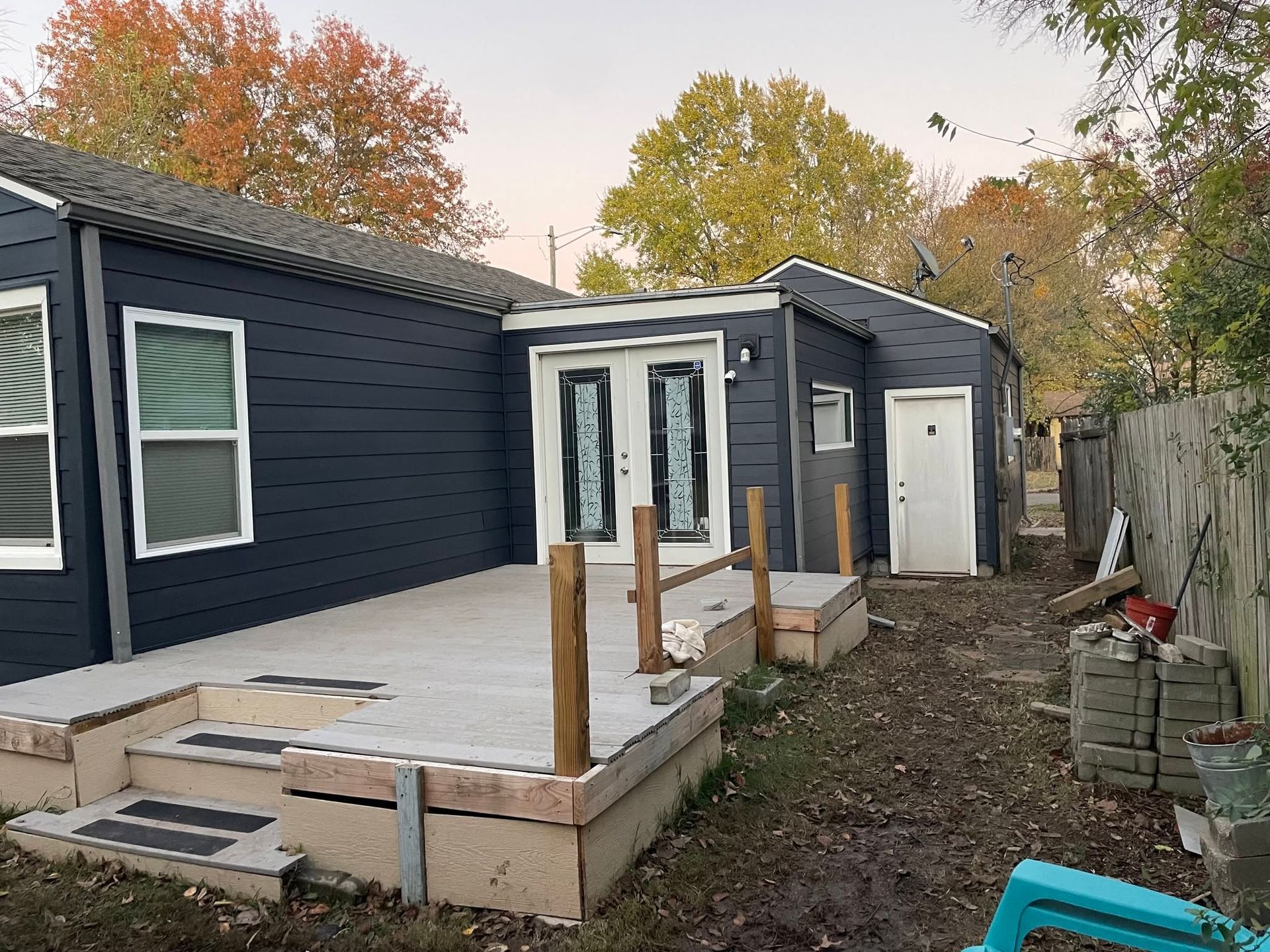 Backyard deck addition beside a dark blue house, with unfinished steps and a white door.