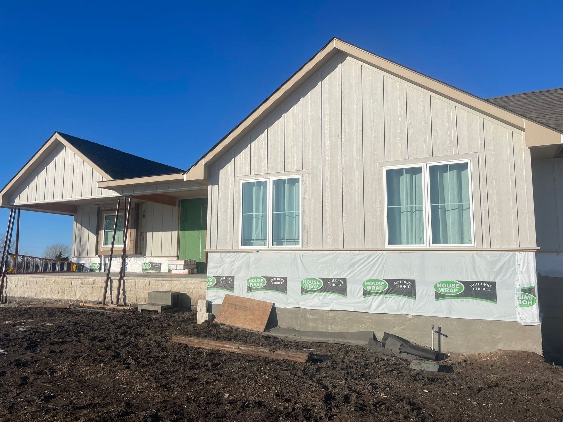 New beige house under construction with porch, white trim, and dark soil in front