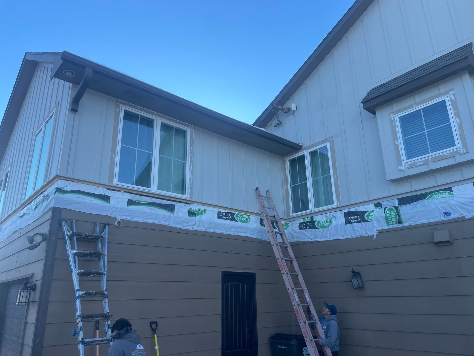 Two workers on ladders painting the exterior of a beige two-story house.
