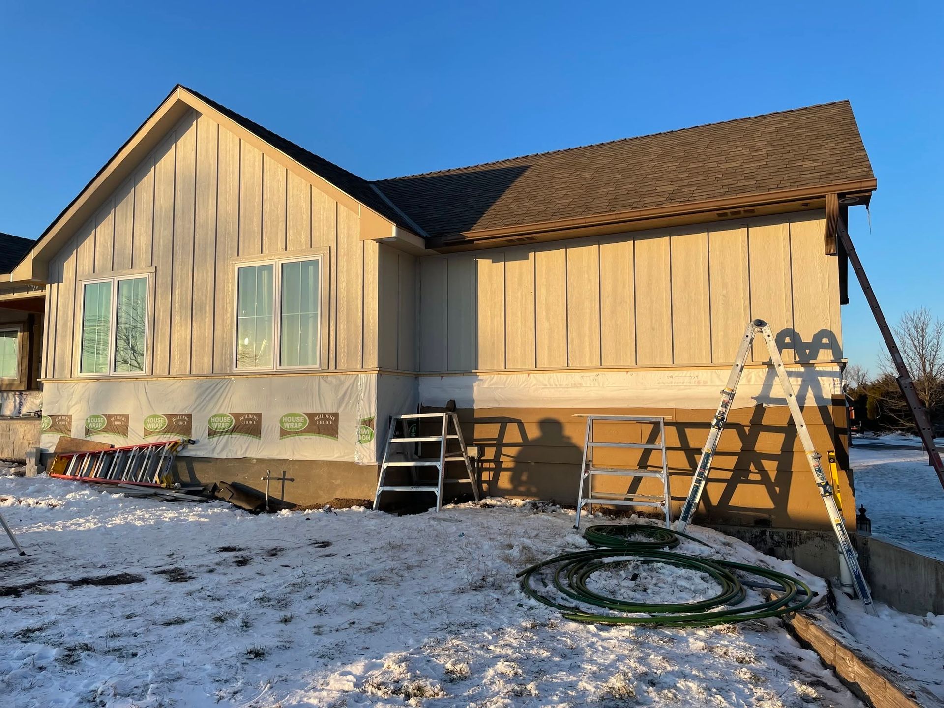 House exterior under renovation with ladders and snow-covered ground at sunset