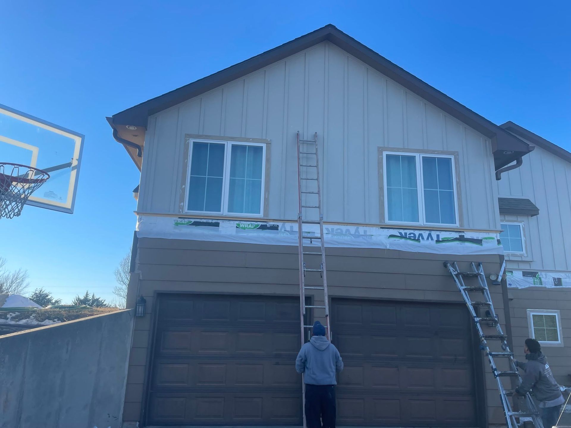 Workers on ladders painting the front of a two-story house with a garage.