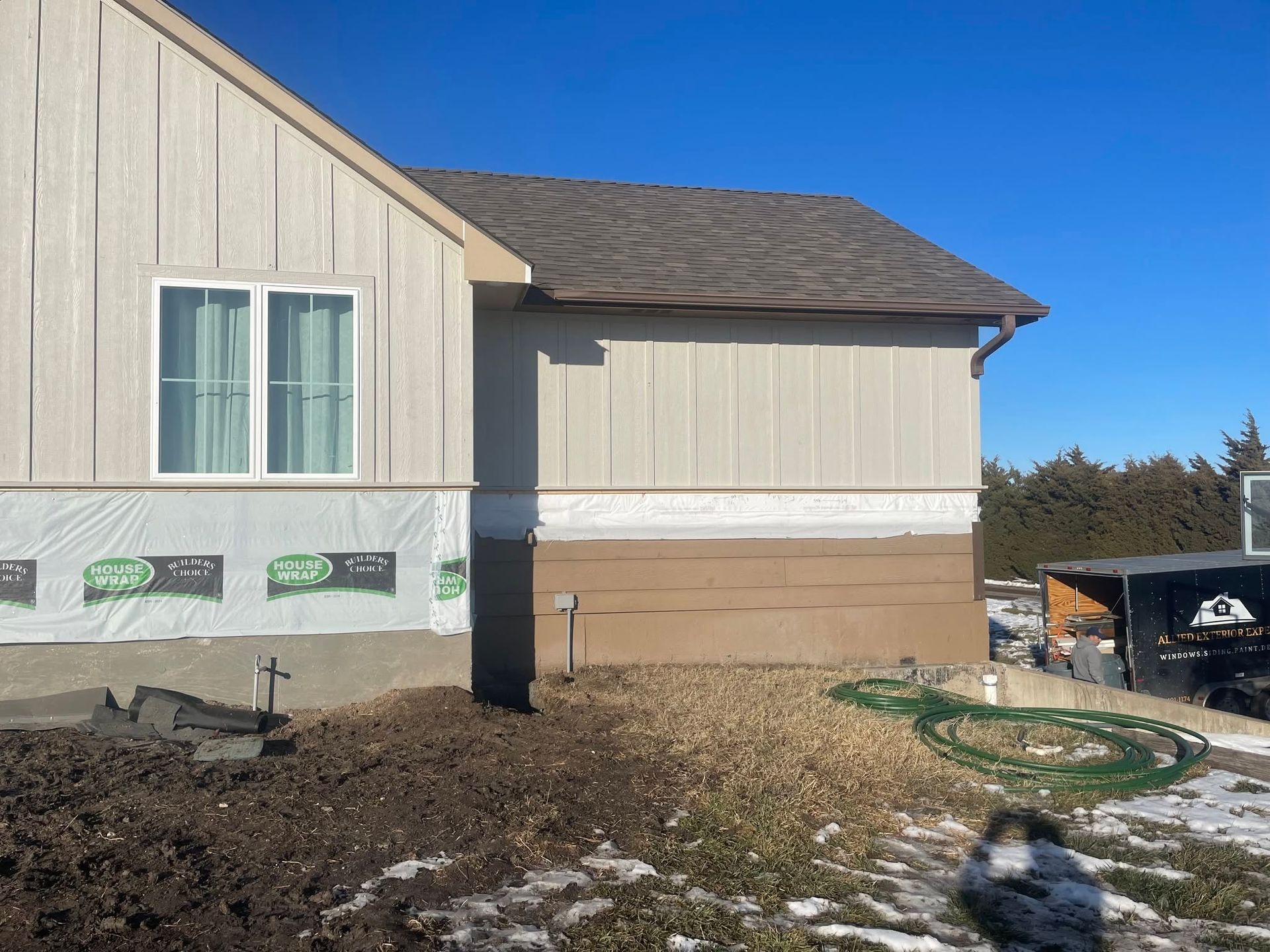 Partly finished house exterior with siding, windows, and bare landscaping under a clear blue sky