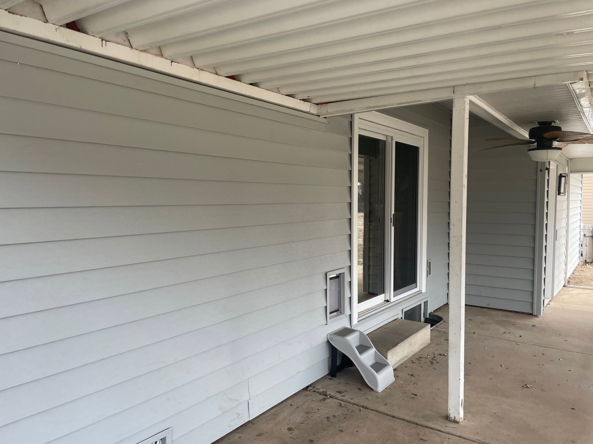 Covered porch with white siding, a window, and a small wall-mounted step stool beside the door.