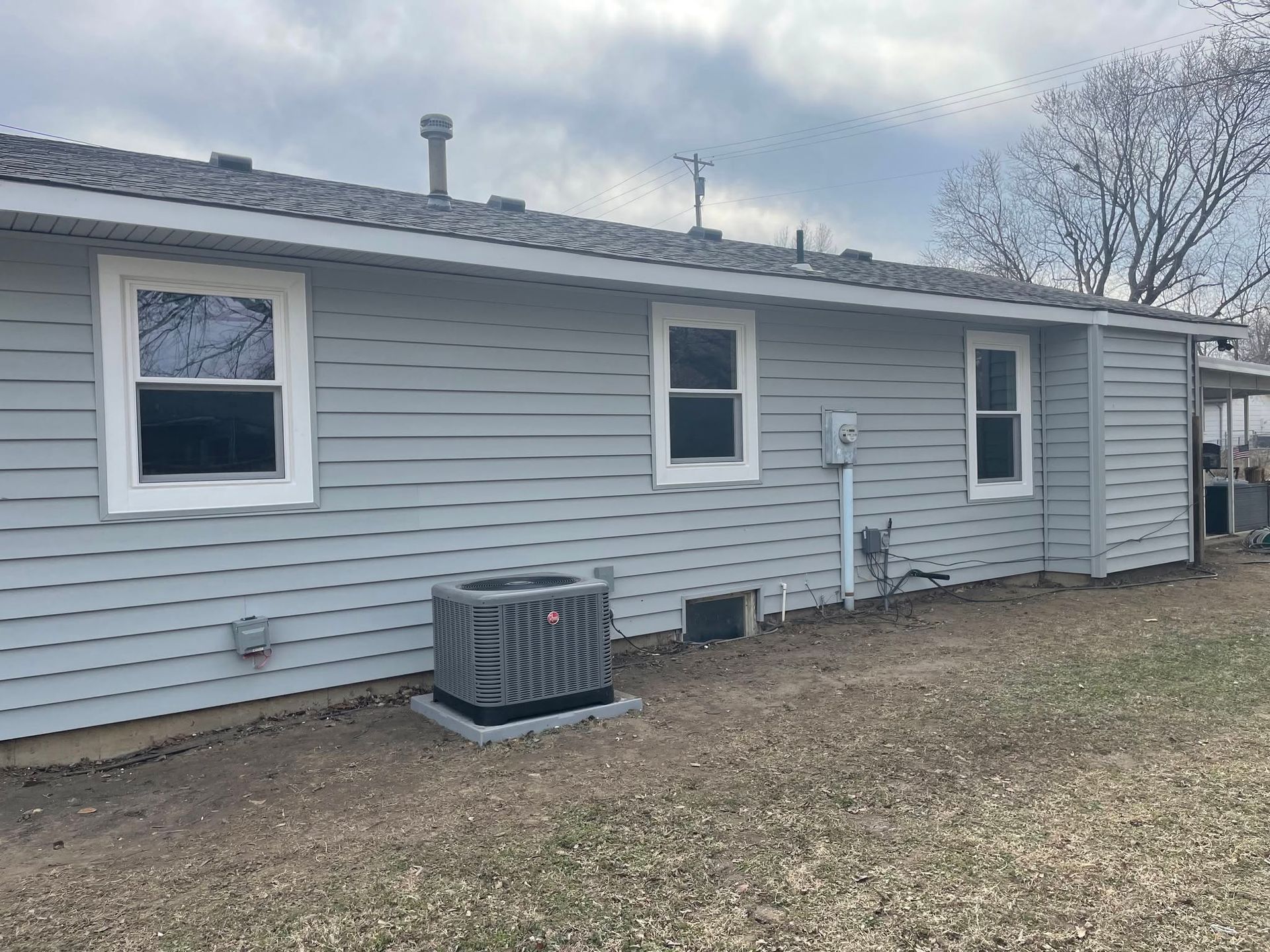 Gray single-story house exterior with three windows, a side door, and an air conditioner unit on the wall.