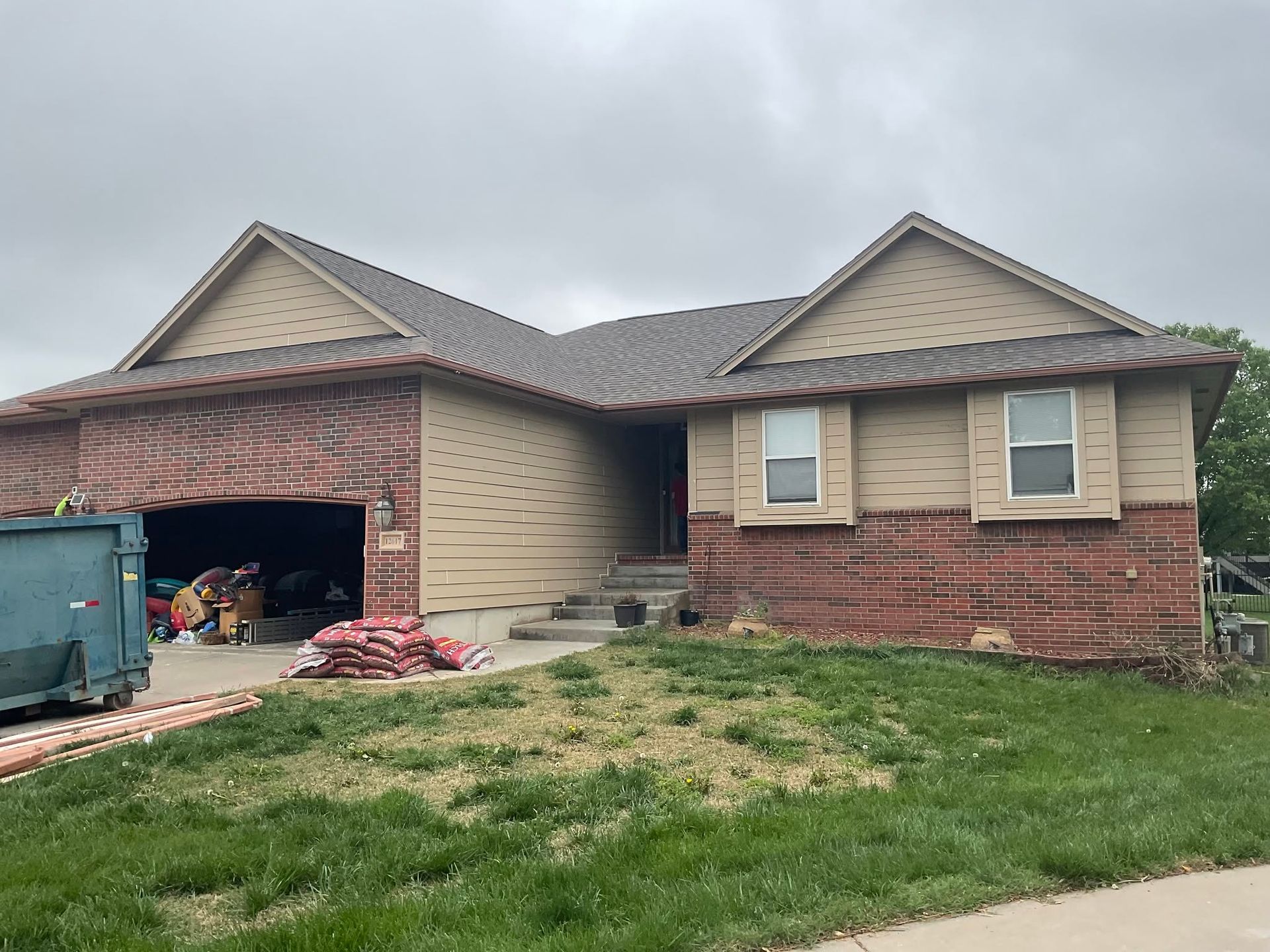 Single-story brick-and-beige house with open garage, overcast sky, and grass in front