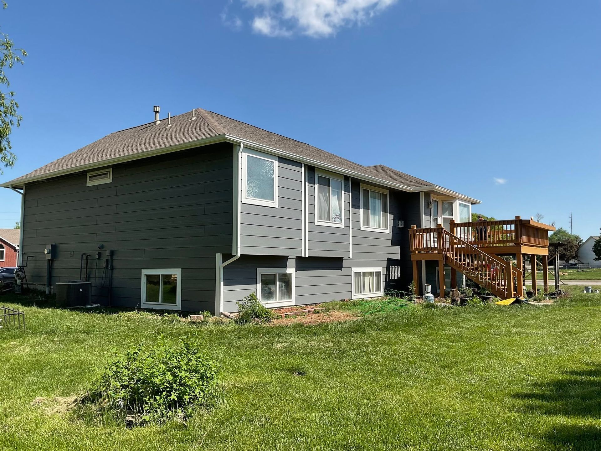 Gray two-story house with a wooden deck in a grassy yard under a blue sky