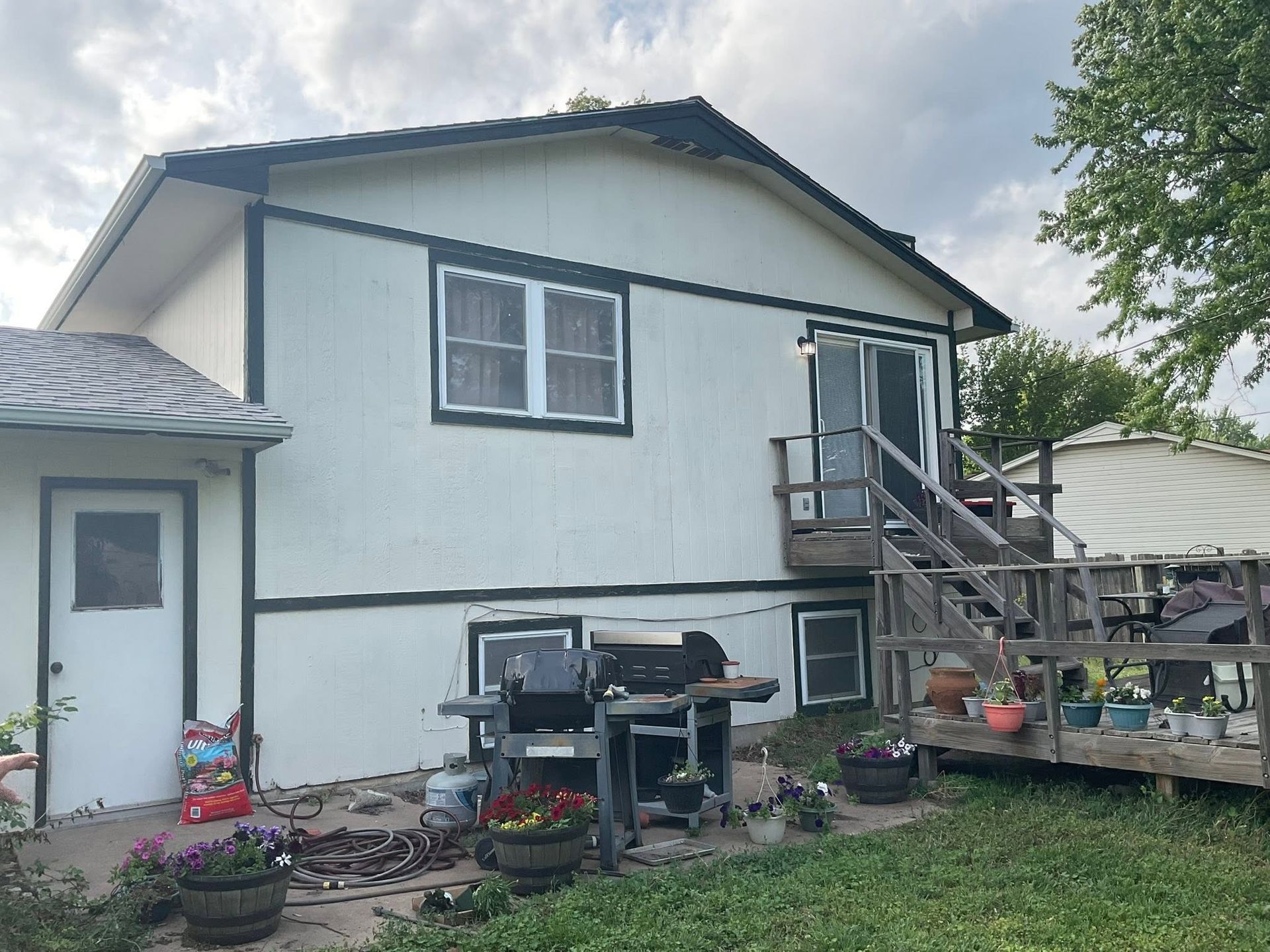 House exterior with white siding, porch stairs, and a backyard patio with grill and potted flowers