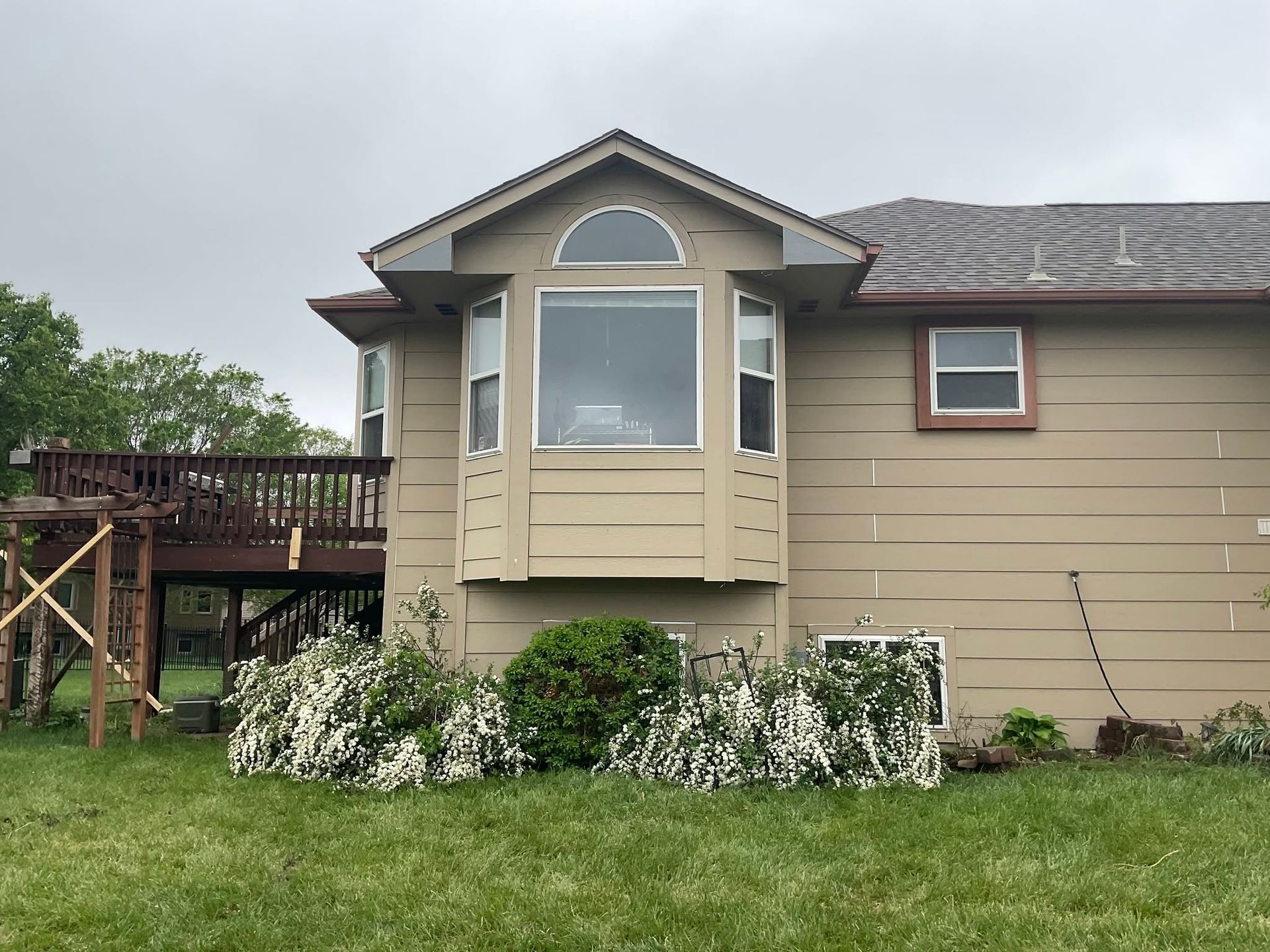 Suburban house exterior with tan siding, bay window, wooden deck, and green lawn