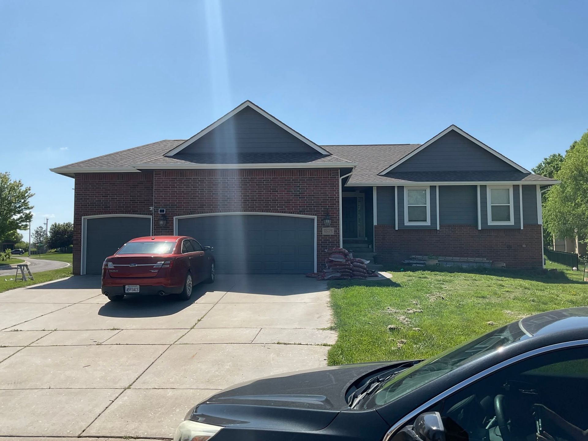Single-story brick house with two garages, a red SUV in the driveway, and a black car in the foreground.