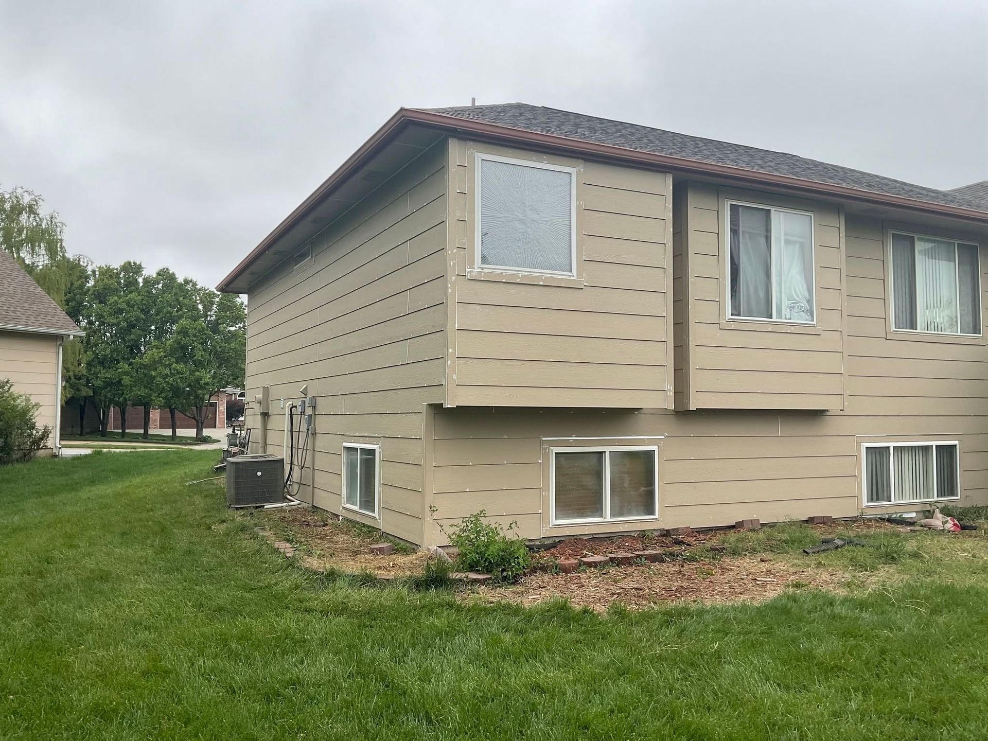 Beige two-story house with white-trimmed windows and a grassy yard on an overcast day