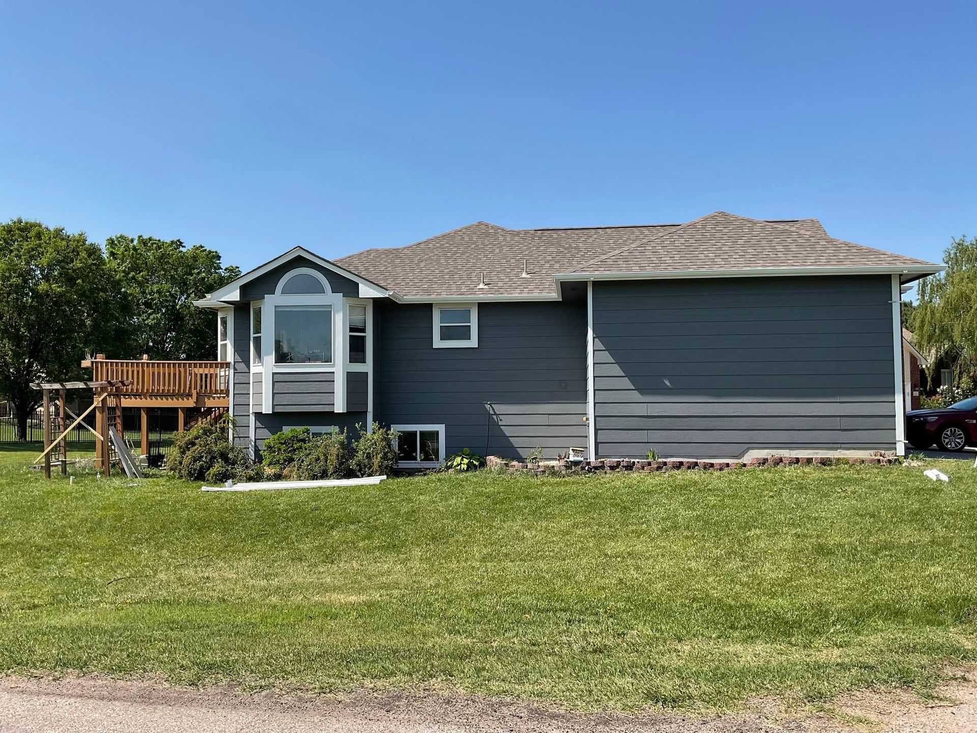 Gray house with a small front porch and wooden deck on a grassy lawn under a blue sky